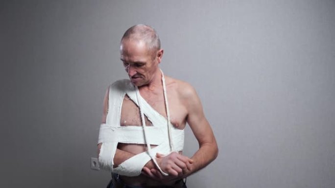 老人用绷带在墙上检查骨折的肩膀