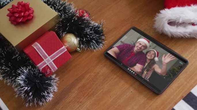 微笑的白人夫妇在平板电脑上的圣诞节视频通话中戴着圣诞老人帽子