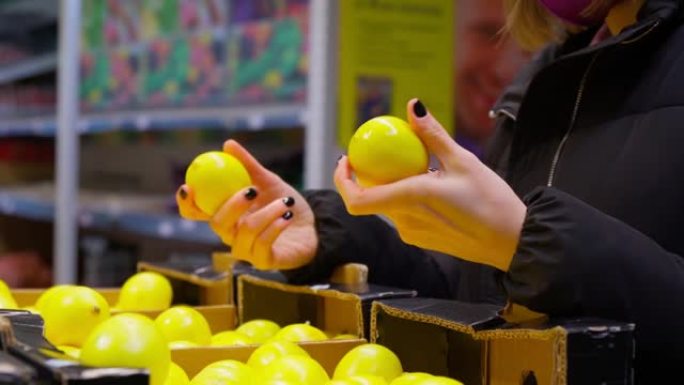 戴面具的女人选择超市里手里拿着柠檬。柑橘类水果是脚气病中维生素c的来源