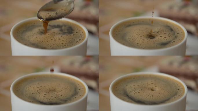 人手搅拌杯热巧克力。新鲜的早晨咖啡特写。慢动作。牛奶热巧克力在白杯。男人在一杯芳香的咖啡特写中搅拌糖
