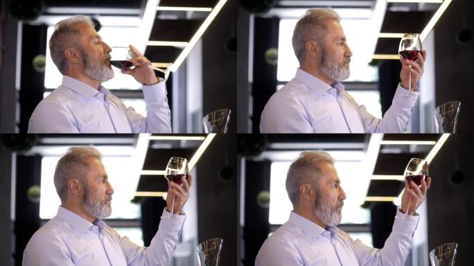 一位老人，胡须，白发，穿着考究的侍酒师，男性酿酒师，品尝香气并检查倒入透明玻璃杯中的红酒的质量。酿酒