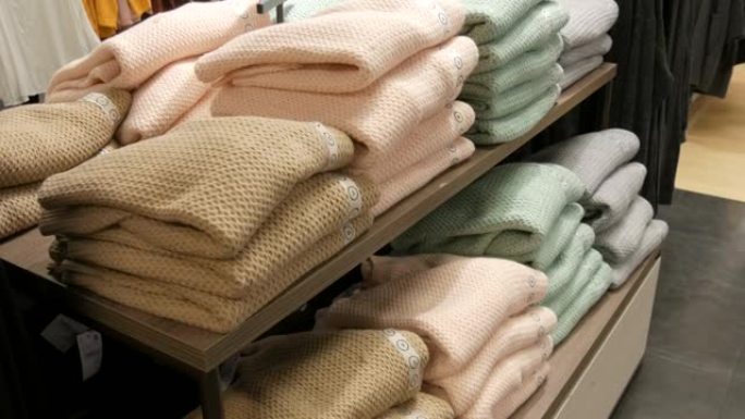美丽温暖的女式浅色针织毛衣在服装店的货架上折叠成一排