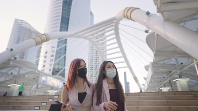 亚洲商务女士在下班后一起在空中行走立交桥上展示城市景观，与最好的朋友一起走回家，年轻的两个同事戴着口