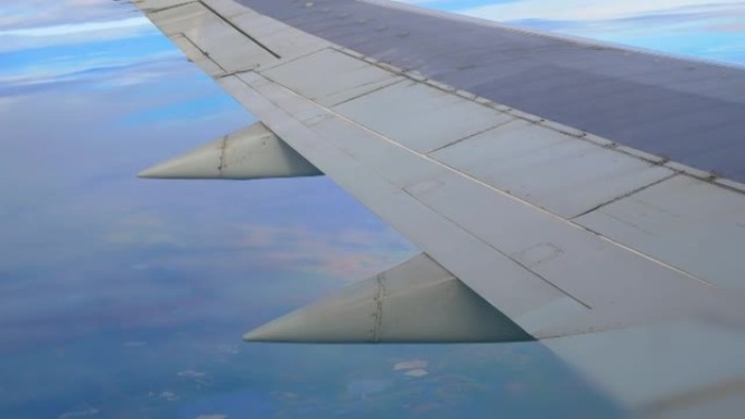 飞机机翼的飞机飞行视图。乘飞机旅行。乘飞机出差。在飞机的机翼下，云层和陆地与湖泊飞逝