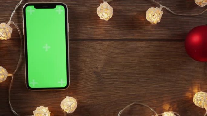 寒假礼物盒子和智能手机绿色屏幕放在木制桌子花环上