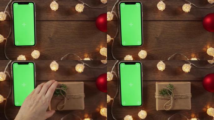 寒假礼物盒子和智能手机绿色屏幕放在木制桌子花环上