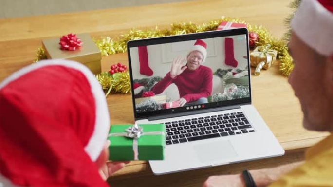 白人父亲和儿子戴着圣诞老人的帽子，使用笔记本电脑与屏幕上的男人进行圣诞节视频通话