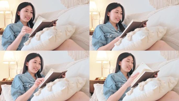 坐在沙发上靠在客厅的亚洲华裔妇女在深夜享受读书