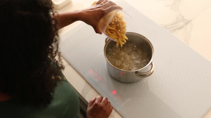 女人将意大利面放在聪明的电磁炉上的沸水中煮