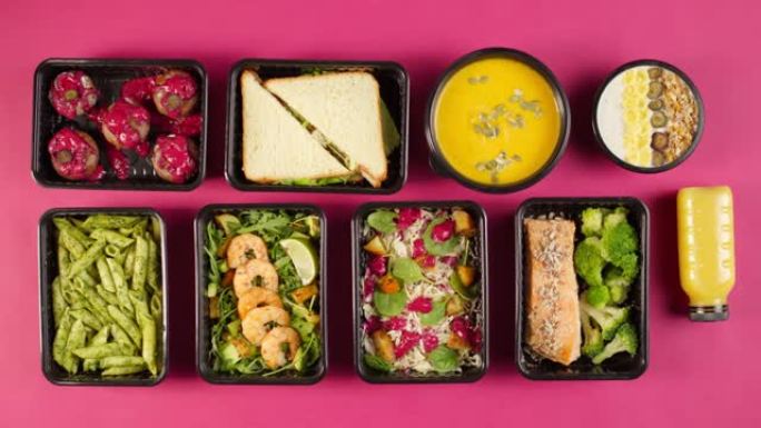 送餐顶视图，在粉红色背景的一次性容器中带走餐点。午餐盒的特写镜头，其中包括煮熟的素食菜肴，在纸杯蛋糕