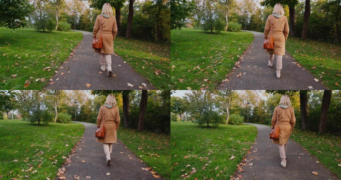 一个穿着外套的女人带着包在秋天的公园里散步，后视