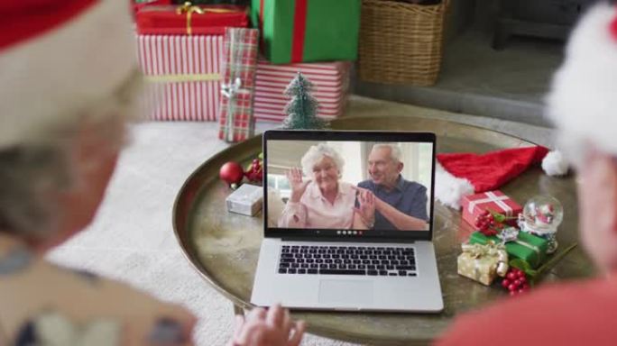 戴着圣诞老人帽子的高级高加索夫妇使用笔记本电脑进行圣诞视频通话，屏幕上有夫妇