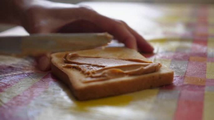 花生酱。用花生酱慢动作制作三明治的女性手。桌子上的面包和花生酱特写。