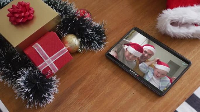 在平板电脑上的圣诞节视频通话中戴着圣诞老人帽子的微笑高加索家庭