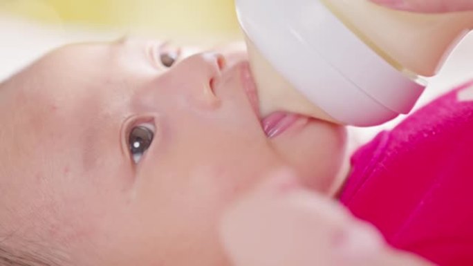 妈妈拿着奶瓶的近手新生儿躺在床上喝奶。可爱的婴儿在家用爱喂奶。新生儿概念