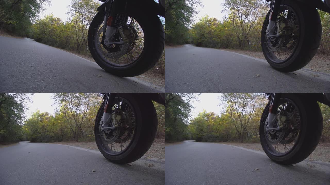 摩托车骑在自然界的道路上。在颠簸的沥青路面上关闭车轮。
