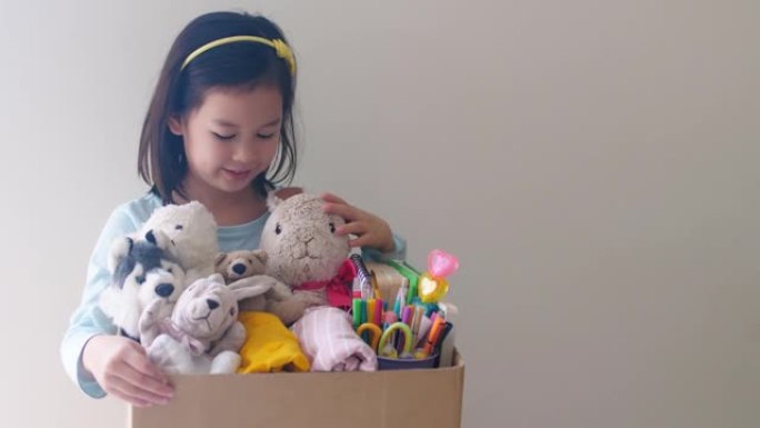 混合亚洲青年志愿者女孩拿着装满旧玩具、衣服、书籍和文具的盒子捐赠快乐慈善、亚洲社区
