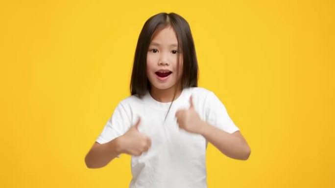 亚洲小女孩在黄色背景上竖起大拇指摆姿势