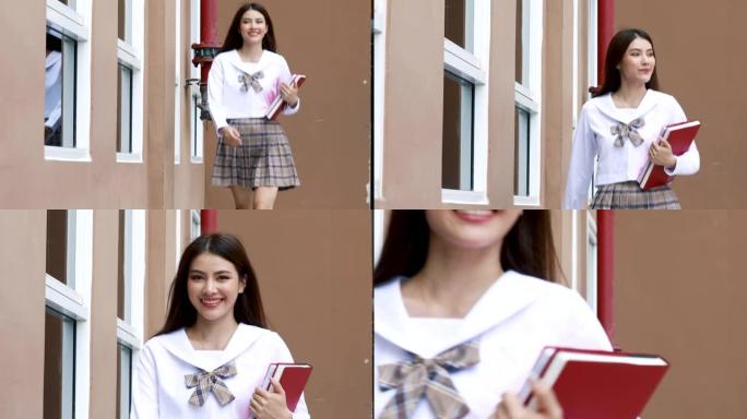 穿着日式大学制服的可爱的年轻女学生拿着书，带着快乐的脸走在shcool大楼前。