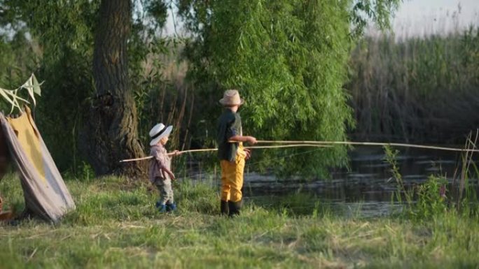 户外休闲，快乐活跃的男孩儿戴着草帽享受他们在一起的时光，在威格瓦姆和绿树的河背景下用钓鱼竿抓鱼