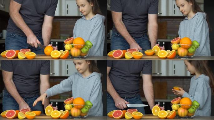 父亲和女儿正在厨房的家中制作新鲜的柑橘汁。小女孩正在舔半个橘子。家庭、幸福与生活理念
