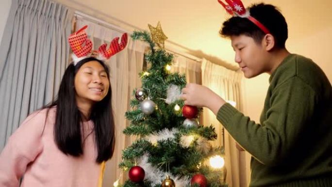 快乐的亚洲儿童戴着驯鹿发带，晚上在家里一起装饰圣诞树，庆祝节日的概念。