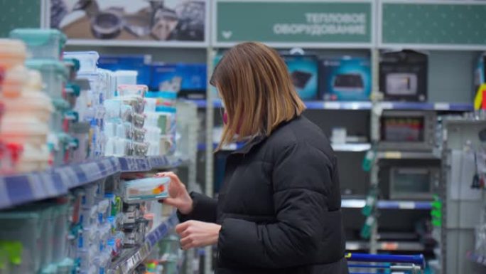 戴着冠状病毒面具的女人在大型超市餐具部门选择商品。选择性聚焦