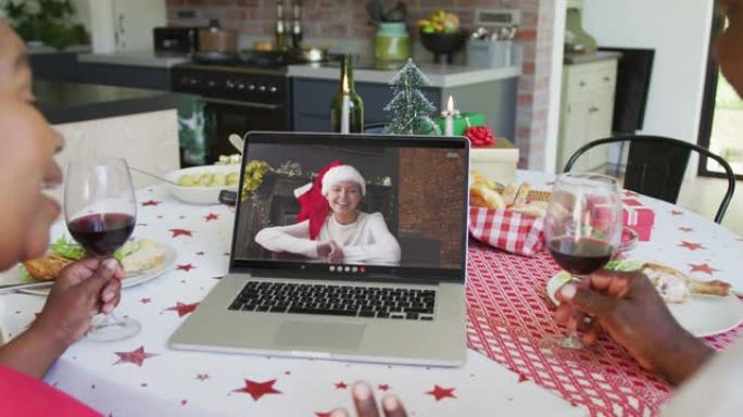 非裔美国人夫妇与葡萄酒使用笔记本电脑进行圣诞节视频通话，屏幕上有幸福女人
