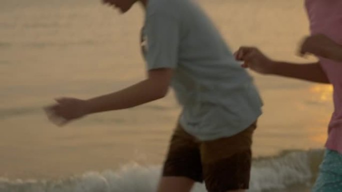 亚洲儿童在沙滩上奔跑，具有日出背景，积极的生活方式理念。
