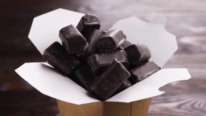 一盒手工巧克力。在纸盒中旋转巧克力糖果。木制背景。