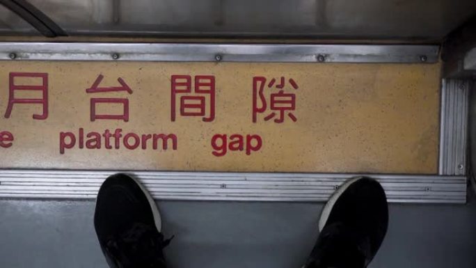 一个人站在火车车厢的门前。特写脚。中文意思是注意平台的差距。火车在行驶，相机摇晃。主题在右边。