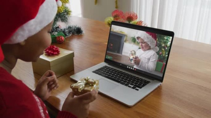 戴着圣诞老人帽子的非洲裔美国妇女使用笔记本电脑进行圣诞节视频通话，屏幕上有男孩