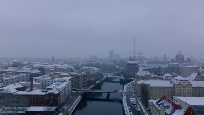 在市中心的施普雷河上空向后飞行。汽车在桥上过水行驶。雪覆盖了海滨的建筑物。德国柏林