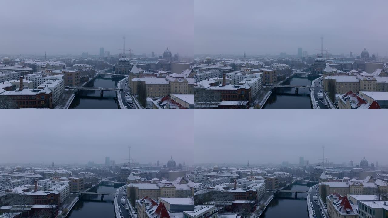 在市中心的施普雷河上空向后飞行。汽车在桥上过水行驶。雪覆盖了海滨的建筑物。德国柏林