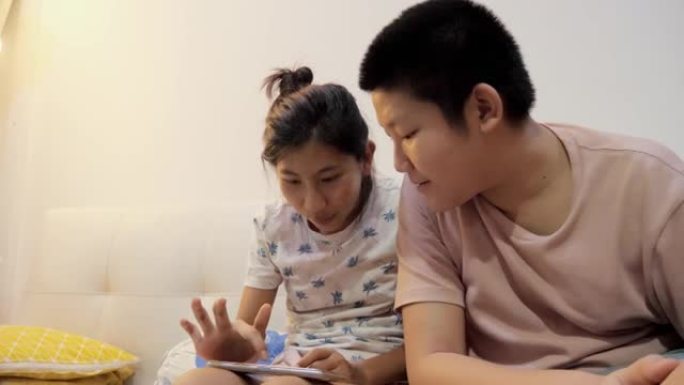 亚洲儿童通过智能手机在沙发上一起观看电影或视频，晚上在家，生活方式概念。
