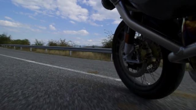 摩托车骑在自然界的道路上。在颠簸的沥青路面上关闭车轮。以100 fps记录。