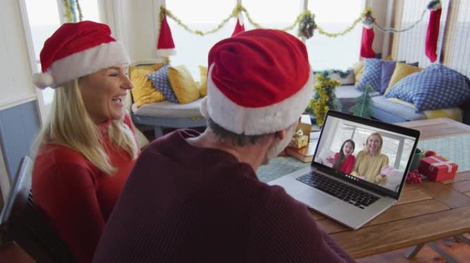 微笑的高加索夫妇戴着圣诞老人的帽子，使用笔记本电脑与家人在屏幕上进行圣诞节视频通话