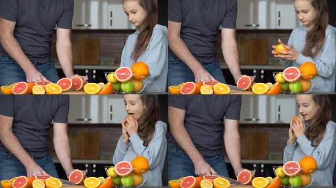 父亲和女儿正在厨房的家中制作新鲜的柑橘汁。小女孩正在舔半个橘子。家庭、幸福与生活理念