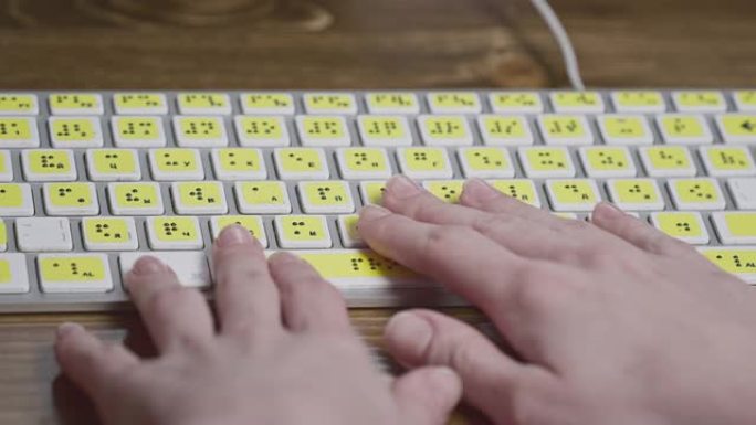 带盲文的电脑键盘特写。一个失明的女孩正在用手在按钮上打字。视障人士的技术设备。