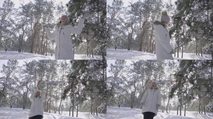 一个穿着冬装的漂亮女孩开心地笑着，享受着寒冷的晴天，呼吸着新鲜的空气。走在白雪皑皑的森林里。松枝上有