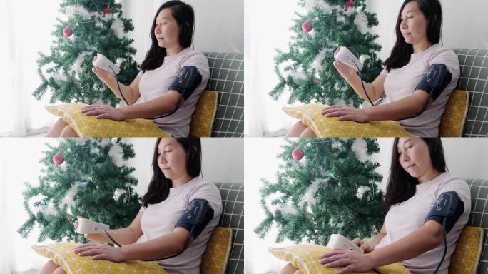 亚洲成年女性在家沙发上的血液加压与圣诞树装饰背景，健康的生活方式理念。