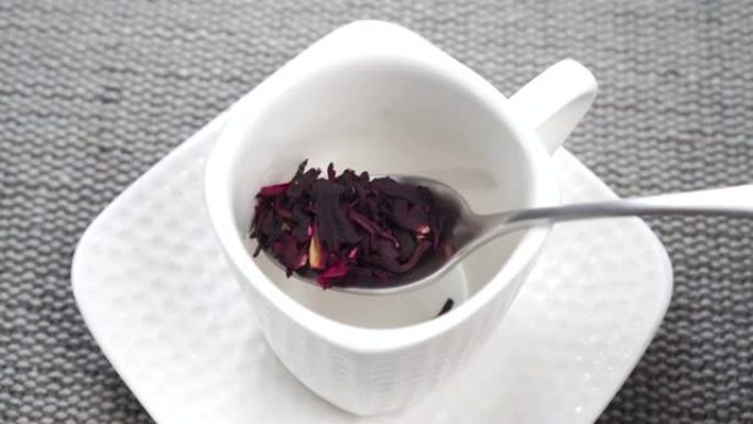 一茶匙将红色的芙蓉茶花瓣放入白色杯子中