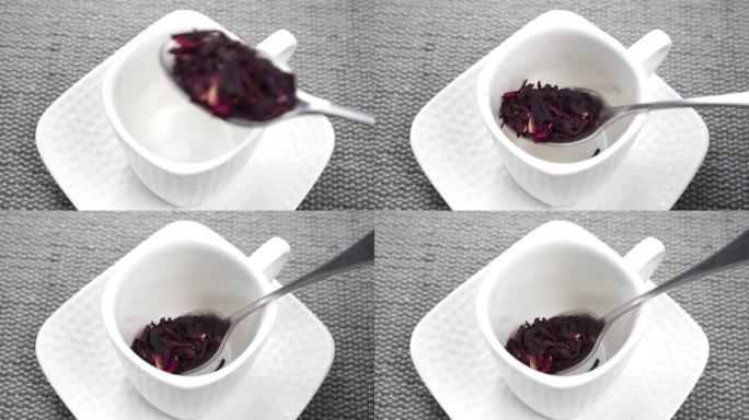 一茶匙将红色的芙蓉茶花瓣放入白色杯子中