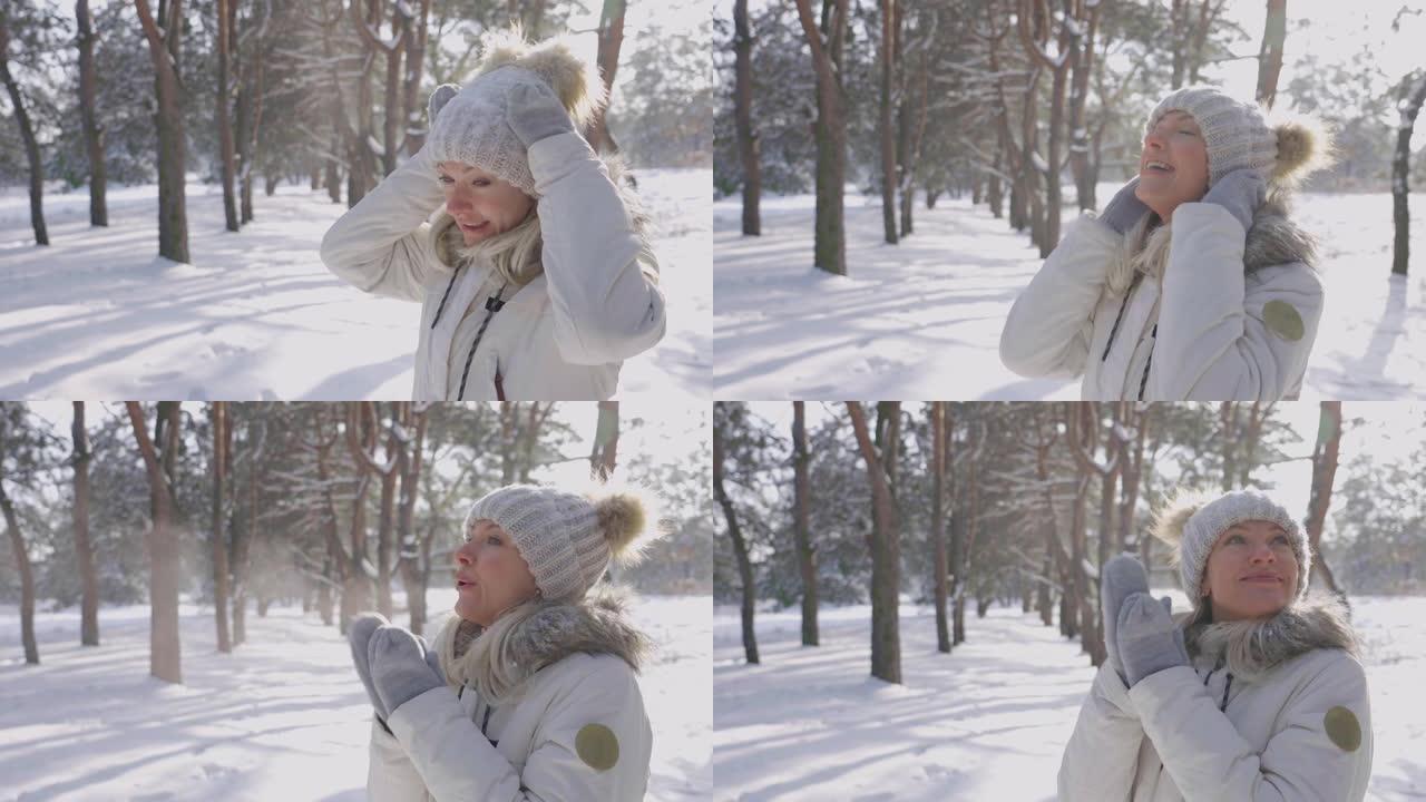 穿着冬衣的可爱女孩的肖像从帽子上压雪，用温暖的手套温暖双手。女孩正在享受寒冷的晴天。美丽的冬季大自然