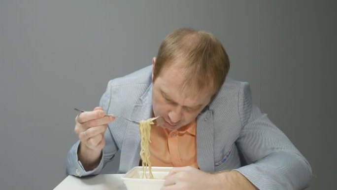 一个穿着夹克和衬衫的男人不想吃方便面。他用叉子挑面条，没有食欲就吃了。