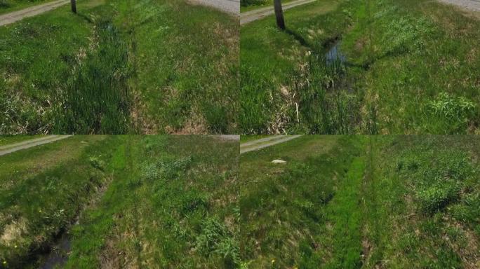 用无人驾驶飞机向前飞行，在沟渠上方覆盖着高高的绿草和底部的一点水
