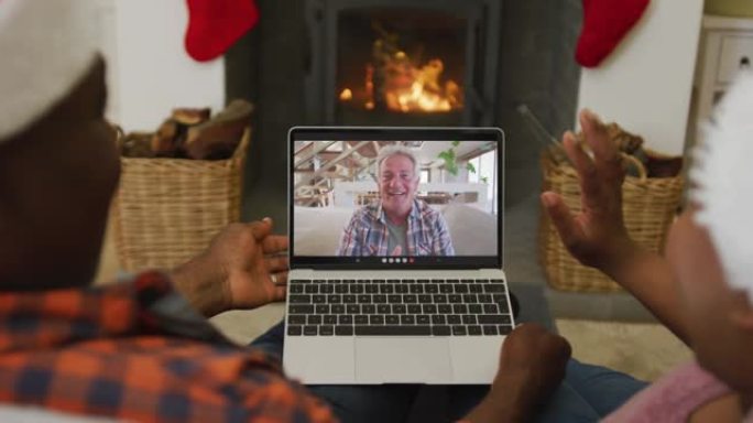 非裔美国人夫妇戴着圣诞老人的帽子，使用笔记本电脑与屏幕上的男人进行圣诞节视频通话