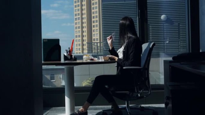 女商人在工作场所吃饭，在全景窗户附近的现代漂亮办公室里，与窗户里的工人，建筑商调情