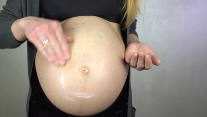 孕妇使用奶油，在肚子上露出微笑。4K