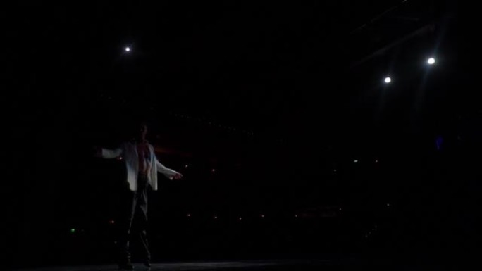 单人表演片段，交际舞舞者在舞台上的白色衬衫，裸露的躯干晒黑。从舞台到黑暗的大厅，后面的聚光灯。跨过去